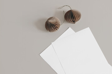 Christmas still life scene. Blank paper sheets mockups on beige table background. Trendy brown Christmas paper ornaments. Winter design, composition. Flat lay, top view.
