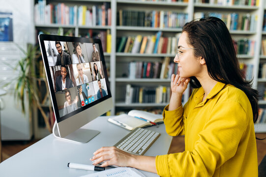 Online education. A female student learning online at home, focused watching at a computer monitor on which a group of other students and a teacher telling information