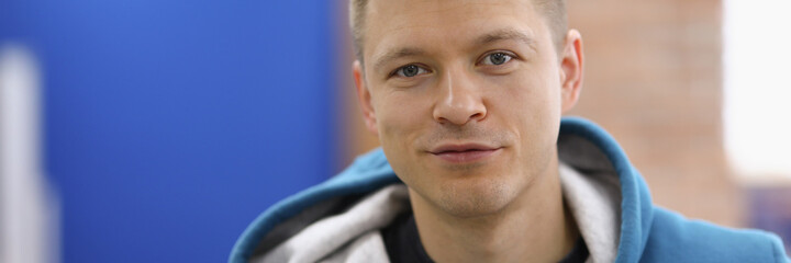 Obraz premium Portrait of smiling cheerful young man posing on camera in room. Happy adult wearing blue hoodie. Copy space in left side. Modeling and happiness concept