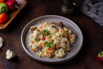 Rice pilaf with meat on a plate on a brown wooden table, decorated with parsley