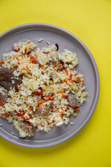 Pilaf from rice and meat on a round plate, top view, bright yellow background.