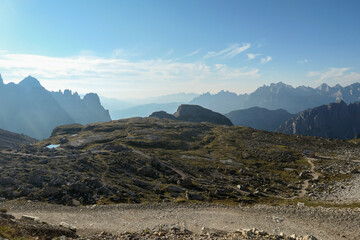 A view on a vast valley in Italian Dolomites. The valley is surrounded with high mountains from each side. Strong, early morning sun. There are a few clouds above. Remote and isolated place. Remedy