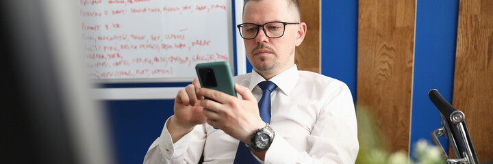 Portrait of middle-aged man wearing posh suit and using mobile phone. Male person reading information on smartphone. Modern technology and personal cabinet concept