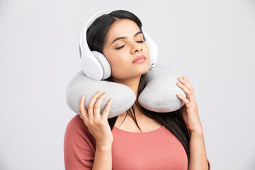 Young woman with a neck pillow with headphones on white.