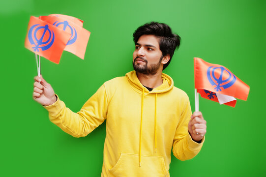 Happy Guru Nanak Jayanti concept. Young indian man in yellow sweatshirt hold flags. Cool south asian guy wear hoodie celebrating India holiday.