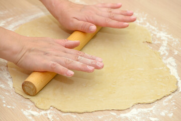Women's hands roll out the dough with a rolling pin