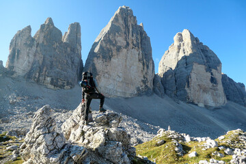 A man standing on a big boulder and enjoying the close up view on the Tre Cime di Lavaredo (Drei Zinnen), mountains in Italian Dolomites. Sharp and high mountain wall. Desolated and raw landscape