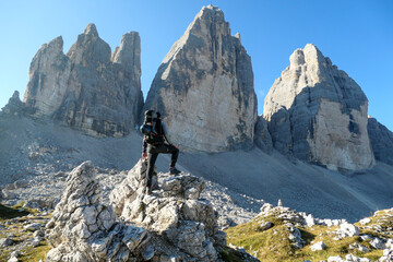 Fototapeta na wymiar A man standing on a big boulder and enjoying the close up view on the Tre Cime di Lavaredo (Drei Zinnen), mountains in Italian Dolomites. Sharp and high mountain wall. Desolated and raw landscape