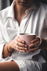 Woman in a white t-shirt holds morning coffee in a pink ceramic cup. Manicure. 