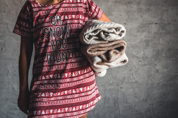 A girl in a Christmas dress holds a stack of sweaters. Warmth, comfort