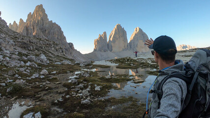 A couple taking a selfie with the Tre Cime di Lavaredo (Drei Zinnen), mountains in Italian Dolomites. The mountains are reflecting in small paddle. Desolated and raw landscape. Early morning. Daybreak