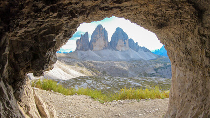 A view from inside a cave on the Tre Cime di Lavaredo (Drei Zinnen) in Italian Dolomites. Peaceful scenery. Steep and sharp mountain peaks. Sunny day. Sneak peaking. Serenity and meditation