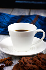 White cup of coffee and chocolate chip cookies on a light wooden table