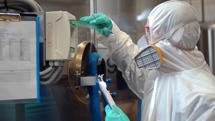 Technologist in white protective uniform and respiratory mask operating on industrial machine