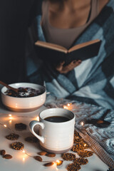 The woman is wrapped in a blanket and holds a book in her hands. cup of coffee . 