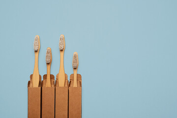 Four natural wooden bamboo toothbrushes in their boxes on a light blue background with copy space and room for text with a left side composition
