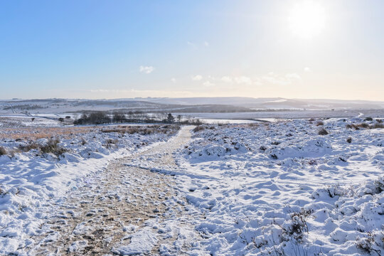 A frozen footpath over a snow covered Derbyshire landscape lit by a low winter sun