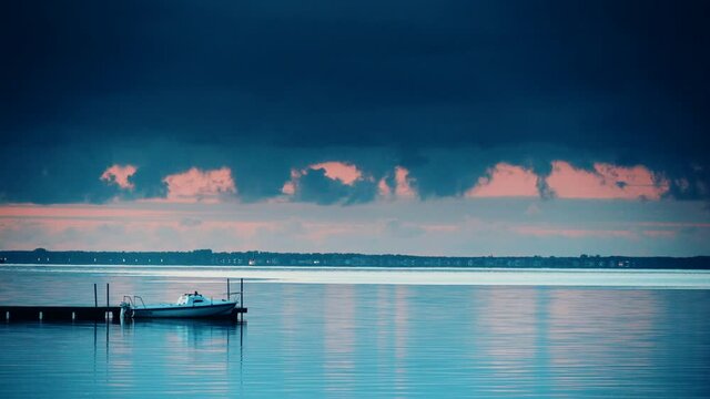 Time lapse of clouds moving over water at evening with boat tied to pier. Baltic Sea, Puck Bay in Poland with Hel Peninsula on horizon. Seaside coast landscape.