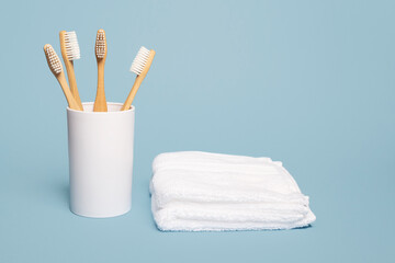 Four wooden natural bamboo toothbrushes in a white cup next to a white cloth on a blue background