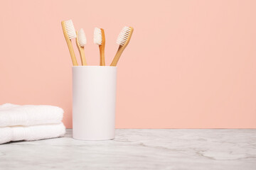 Four natural wooden bamboo toothbrushes in a white cup next to a white cloth on a marble surface...