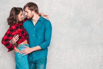 Hot beautiful woman and her handsome boyfriend. Models posing near gray wall in jeans clothes. Young passionate couple hugging before having sex. Sensual pair getting closer for kiss. Lover couple
