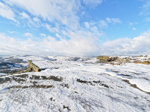 Snow on the rocks of Curbar Edge under gathering clouds in a blue sky
