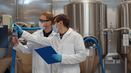 Men with clipboard wearing lab coat and protective mask working at craft brewery