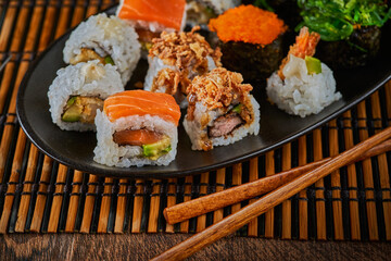 Assortment of Japanese sushi set, gunkan, uramaki, maki, wakame in ceramic plate with soy sauce and chopsticks on bamboo mat. Close up. Selective focus. Japan menu.