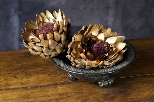 Two dried cardoon heads in a ceramic bowl on a wooden table top
