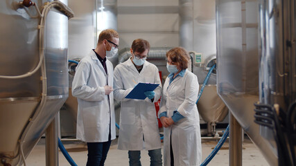 Group of young inspectors in white coat and safety mask conducting audit at beer factory.