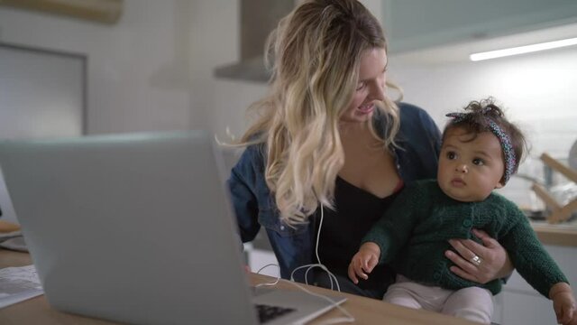 Young woman teleworking from home and watching baby girl 