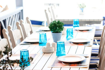 Restaurant with served table. Greek tavern with white wooden chairs by the Mediterranean sea coast, Greece.