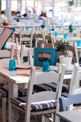 Restaurant with served table. Greek tavern with white wooden chairs by the Mediterranean sea coast, Greece.