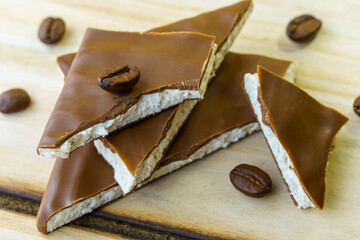 Pieces of chocolate with a white filling inside lie in a heap one on top of the other, sprinkled with coffee beans on a wooden background.