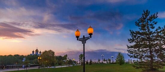 City embankment with burning lanterns in the summer evening against the sunset sky