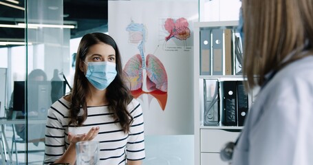 Close up of female young pretty patient in medical mask sitting in doctor office on consultation...