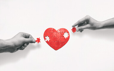 Two people put together a heart-shaped puzzle. The concept of building love relationships. - obrazy, fototapety, plakaty