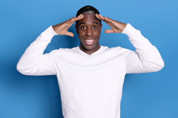 Indoor photo of a young African American man pictured isolated on blue background with hands on head