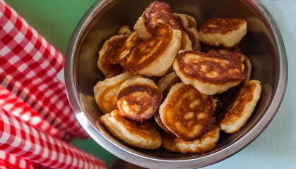 Fried dough pancakes close up in a metal dish and a red checkered curtain on a blue table background