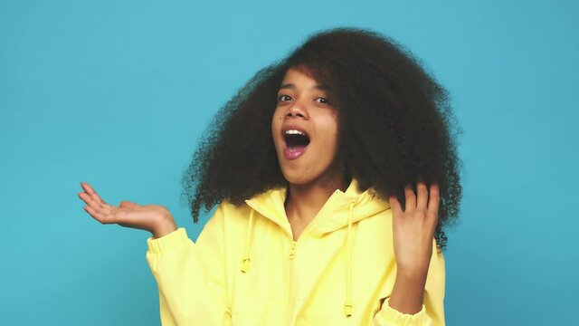Young african american curly woman impressed holding copy space on palm