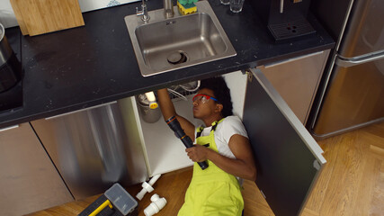 High angle view of african male plumber in overall fixing sink pipe