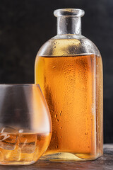 bottle and glass with whiskey or Bourbon Scotch on the table, drops on the glass dark background....