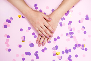 Obraz na płótnie Canvas Stylish women's manicure in pink tones on a background with multicolored confetti