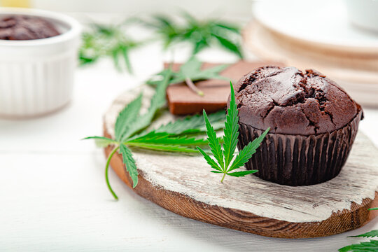 Weed muffins with cannabis on top, cannabis leaves, hemp branches on white table. Marijuana chocolate cupcake muffins with weed cbd. Medical marijuana hemp drugs in food dessert. Copy space