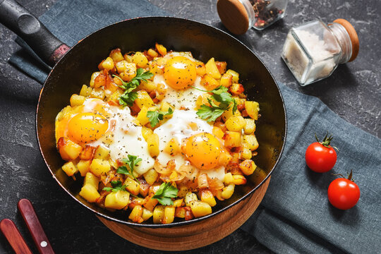 Potato hash with eggs and herbs for breakfast on black stone background