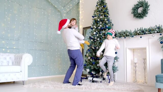 Dad dances with his little son while enjoying Christmas together in an ornate room at home with brightly lit lights and a Christmas tree.