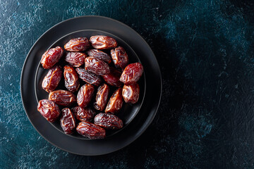 Dried sweet dates on a black plate.