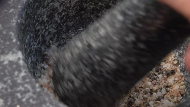 Super close-up of pestle crushing and mixing salt and spices in the grey stone mortar