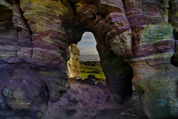 View through a cave with colorful lines of sandstone. located in Crail, Fife, Scotland.