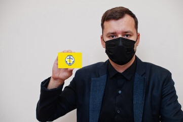 American man wear black formal and protect face mask, hold Anchorage flag card isolated on white...